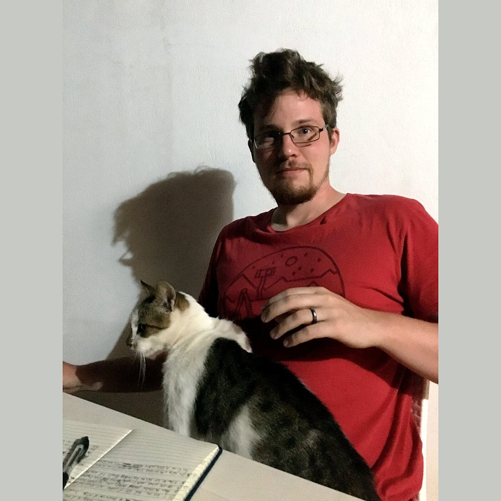 Nate Spanos at home with a cat and an open notebook